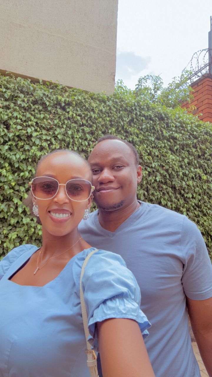Brian and Angella smiling side by side in front of a wall of green ivy